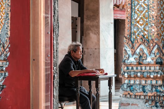 An elderly man sits thoughtfully in a vibrant Bangkok temple, capturing cultural essence.