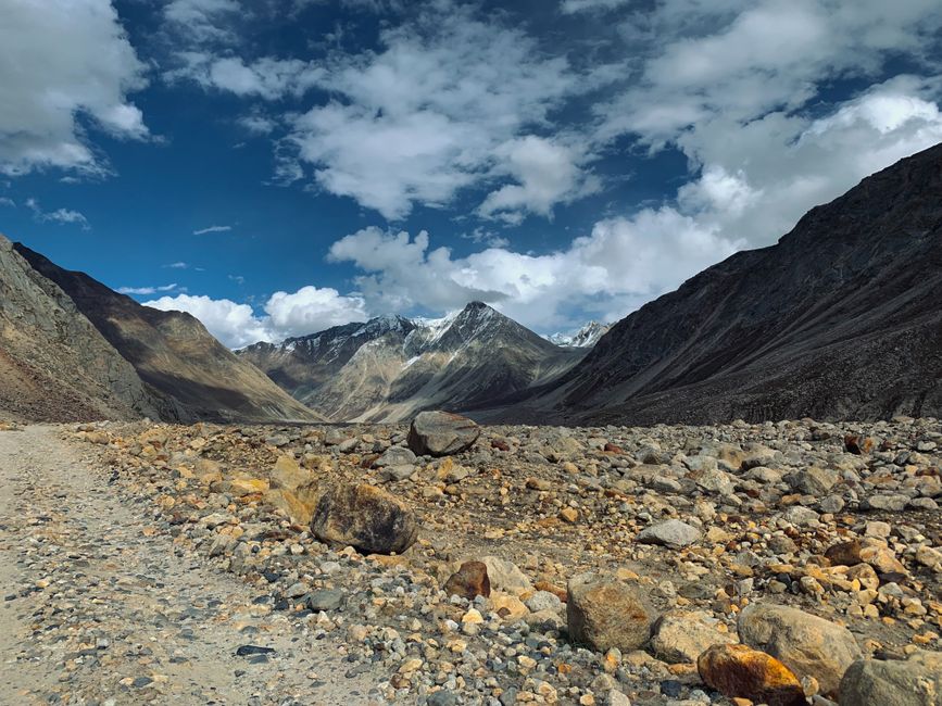 A rugged mountain range under a blue sky with rocky terrain in the foreground.
