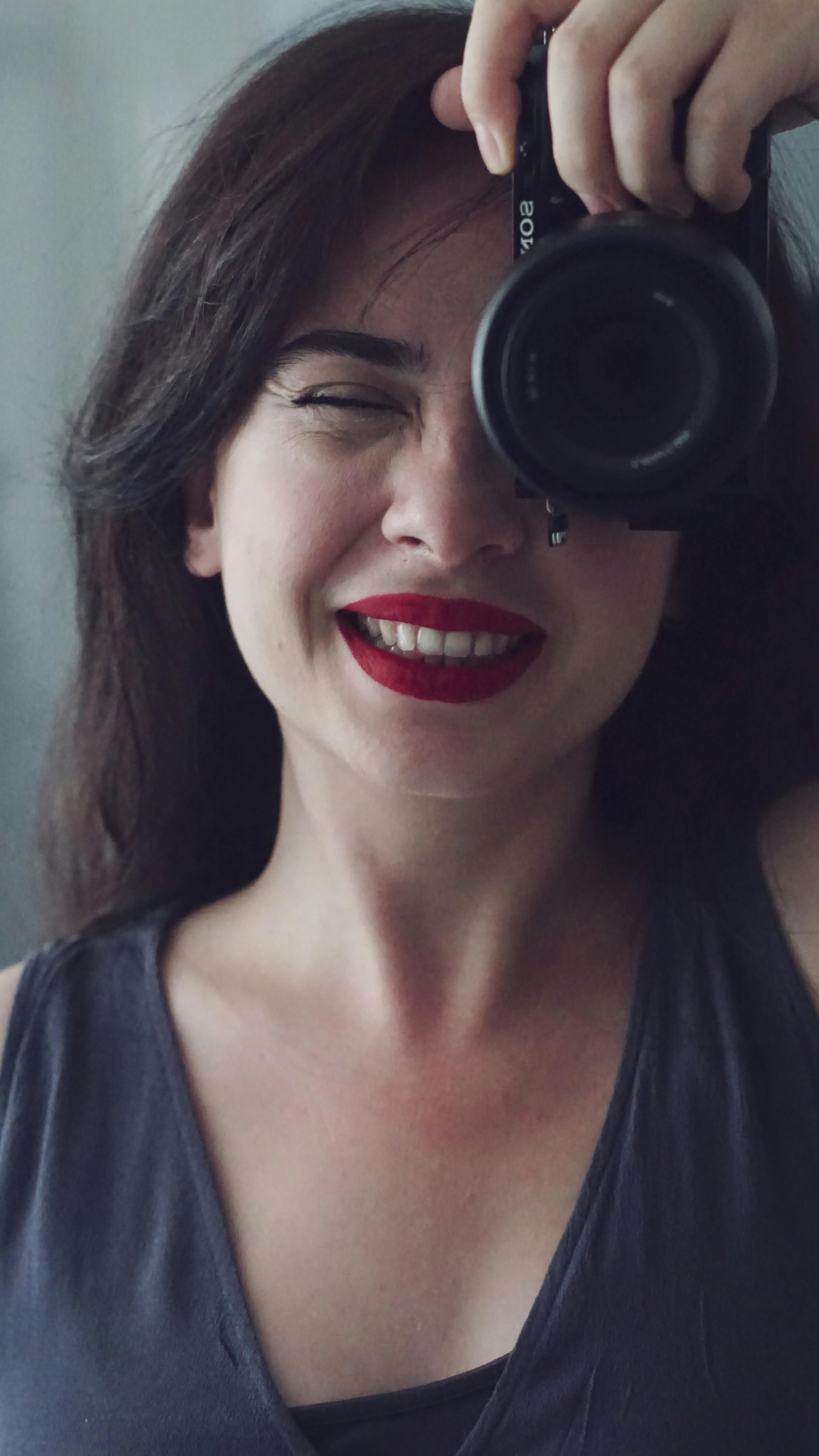 Smiling woman in sleeveless top takes a selfie with a camera, capturing joy and confidence.