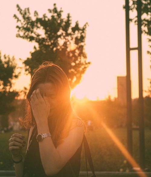 Free A woman stands in an urban park with the sunset creating a warm glow around her. Stock Photo