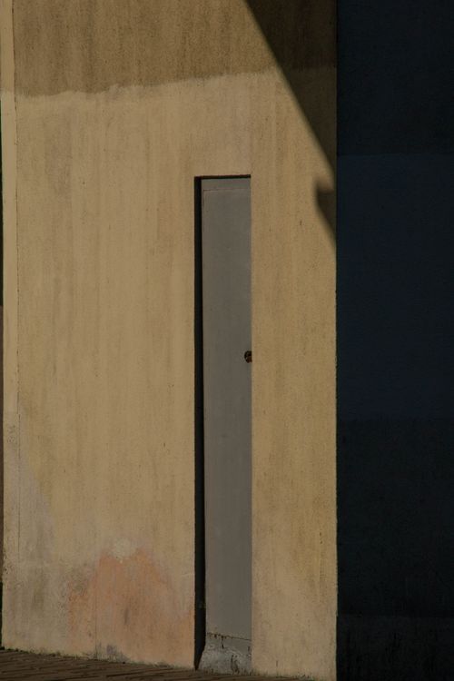 Free A minimalist sunlit wall featuring a narrow vertical door casting shadows. Stock Photo