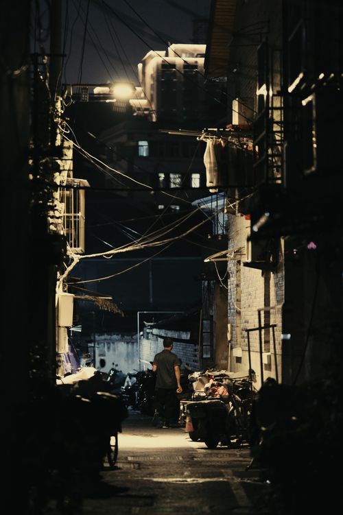 Free A dimly lit urban alleyway at night featuring a lone man and motorcycles. Stock Photo