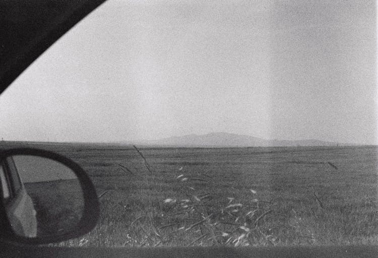 Analog Black And White Photo Of A Grassland Plane Seen Through A Car Window