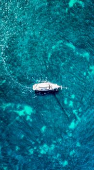 Aerial shot of a yacht sailing through vibrant turquoise waters, creating a serene travel scene.