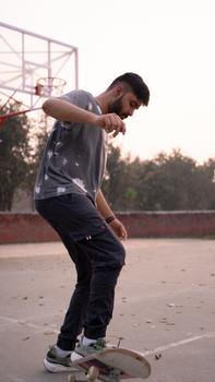 Teenager skateboarding on an outdoor basketball court at dusk.