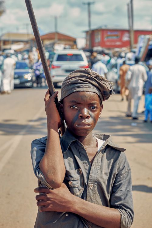 Free A child holding a stick stands on a busy urban street, capturing the essence of city life. Stock Photo