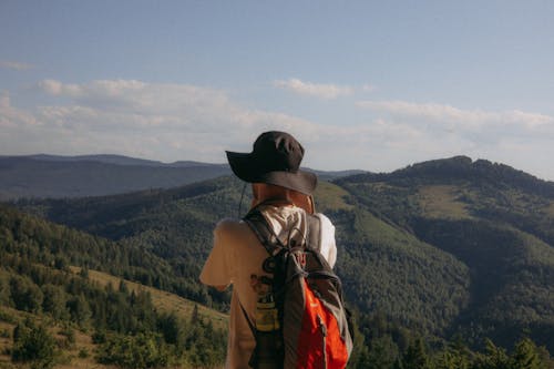 Man in Hat and with Backpack Standing with Hills behind