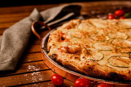 Close-up of a rustic zucchini pizza with cherry tomatoes on a wooden table.