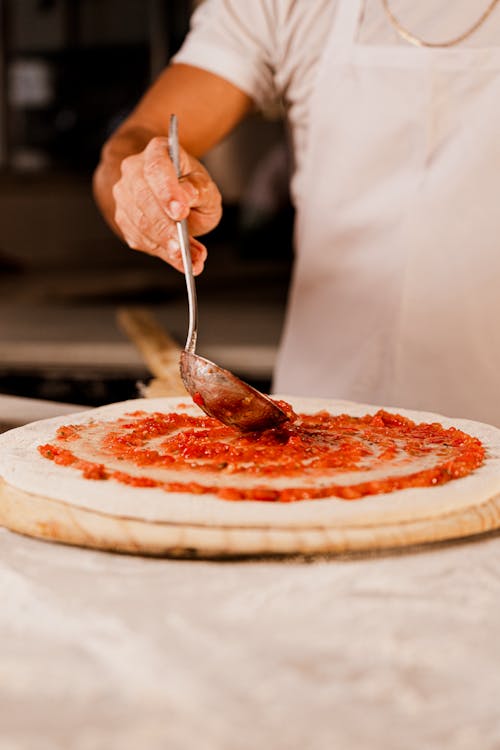 Man Adding Sauce to Pizza