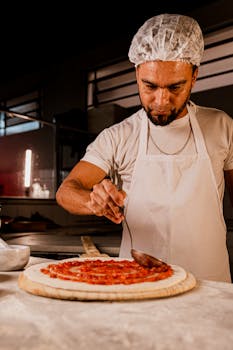 Chef in kitchen spreading tomato sauce on pizza dough with precision