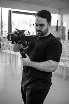 A black and white image capturing a filmmaker with a camera indoors.