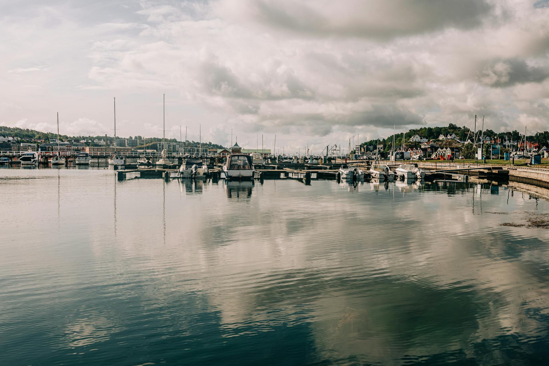 Serene harbor scene with boats moored in a marina, reflecting on calm waters under a partly cloudy sky.