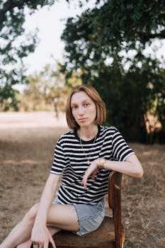 A young woman in casual attire poses on a chair in an outdoor setting.