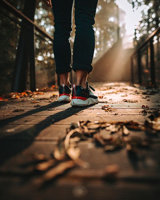 A man walks across a wooden bridge covered with autumn leaves during sunrise, capturing a stylish morning moment.