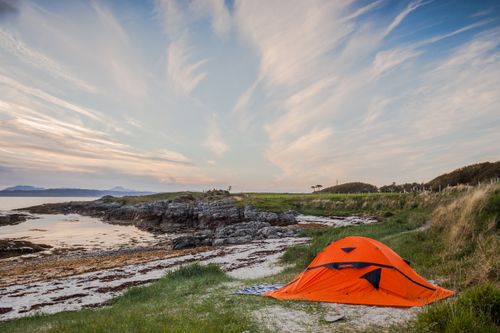 Free Orange tent set by the serene coast in Highland, Scotland during calm summer evening. Stock Photo