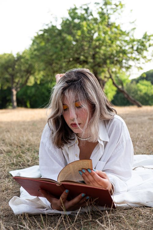 Free Young woman in white enjoying a book on a sunny day in a serene countryside setting. Stock Photo