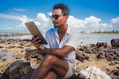 Man in Shirt Sitting with Tablet on Sea Shore