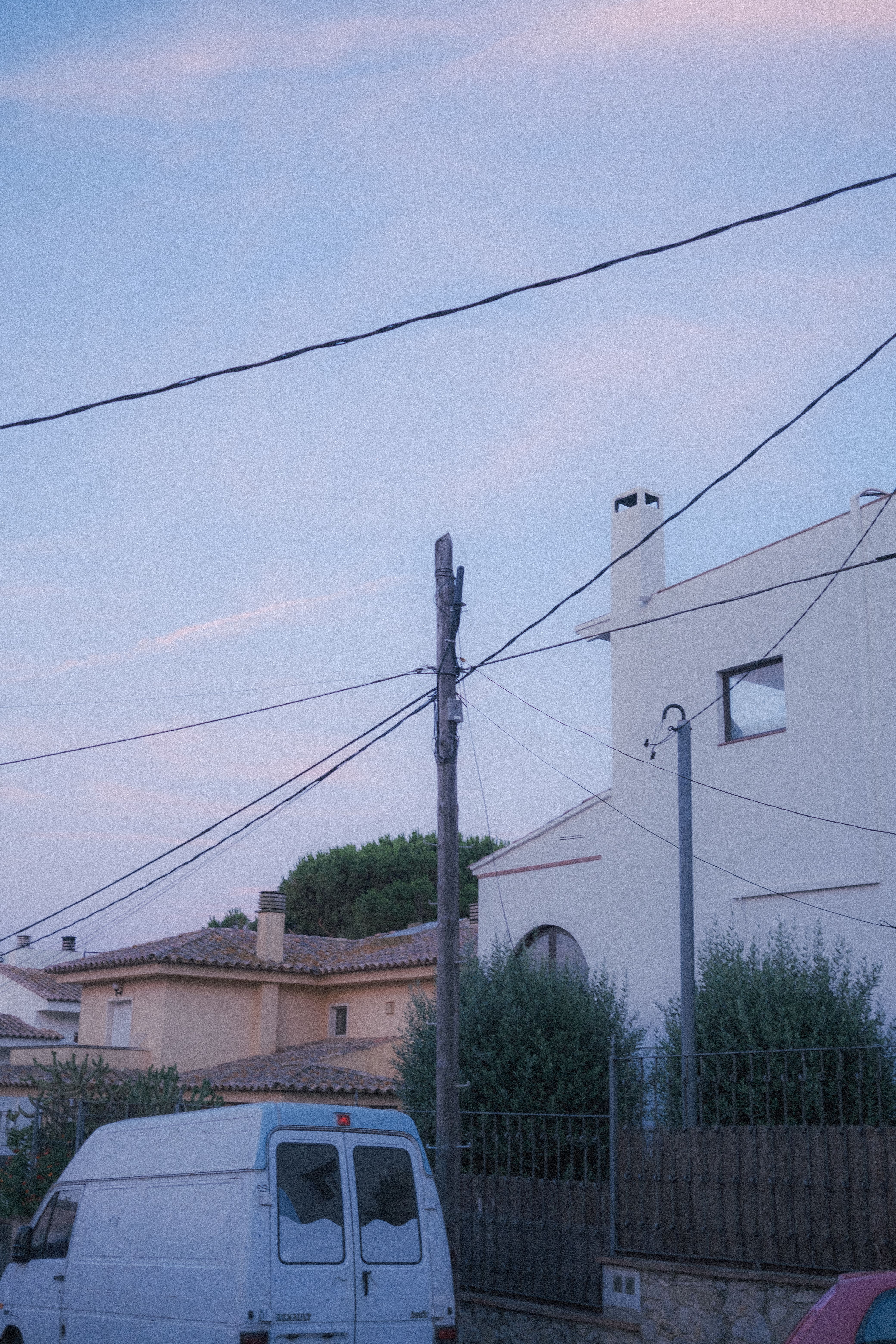 A serene suburban street scene featuring utility poles, a van, and houses under the evening sky.