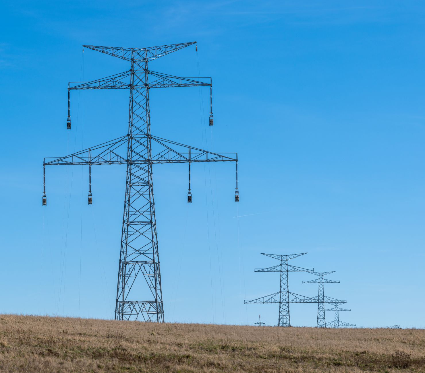 Blue sky over transmission towers on a rural landscape, symbolizing energy distribution.