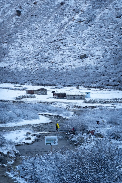 Hikers on a Narrow Footbridge over a River in a Snowy Valley