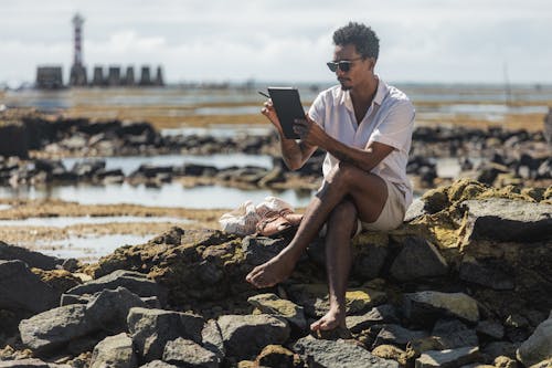 Man in Shirt Sitting with Tablet on Stones