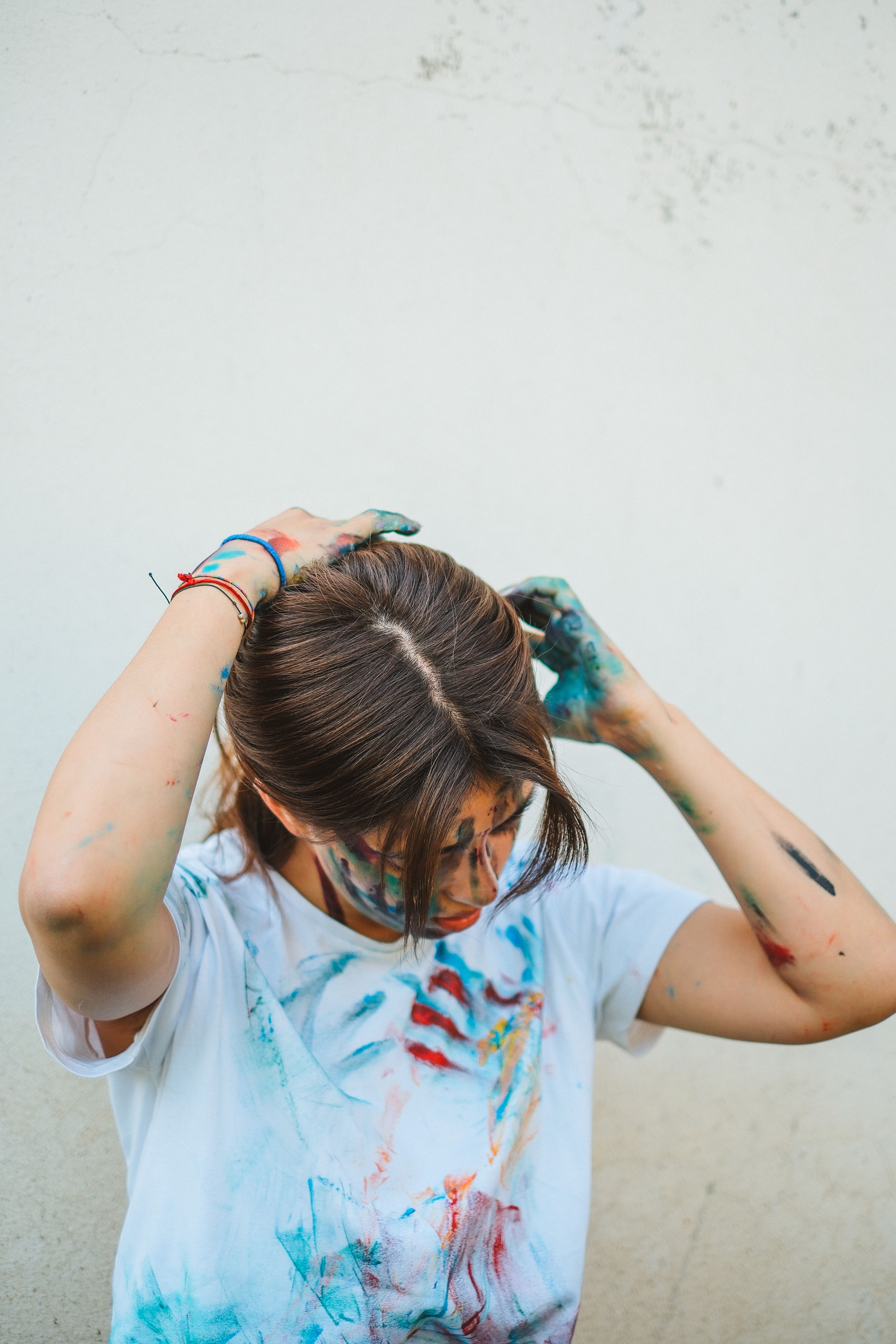 Creative teenager with paint-stained shirt adjusting hair, showcasing artistic expression.