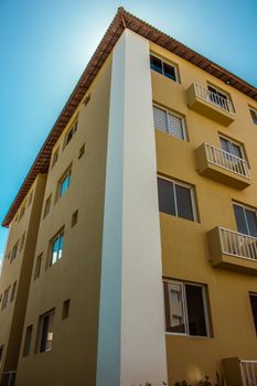 Yellow residential building with windows and balconies under clear blue sky.