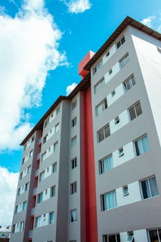Brightly lit modern apartment building with a red accent wall under a clear blue sky.