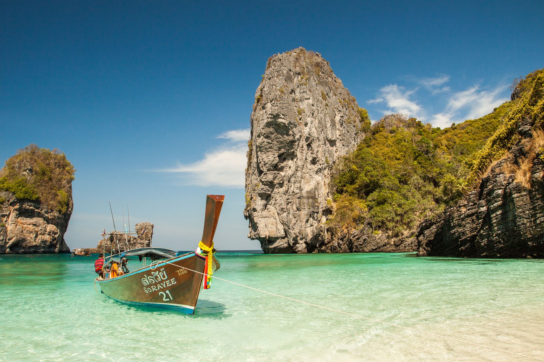 A small boat anchored beneath limestone cliffs in calm turquoise water
