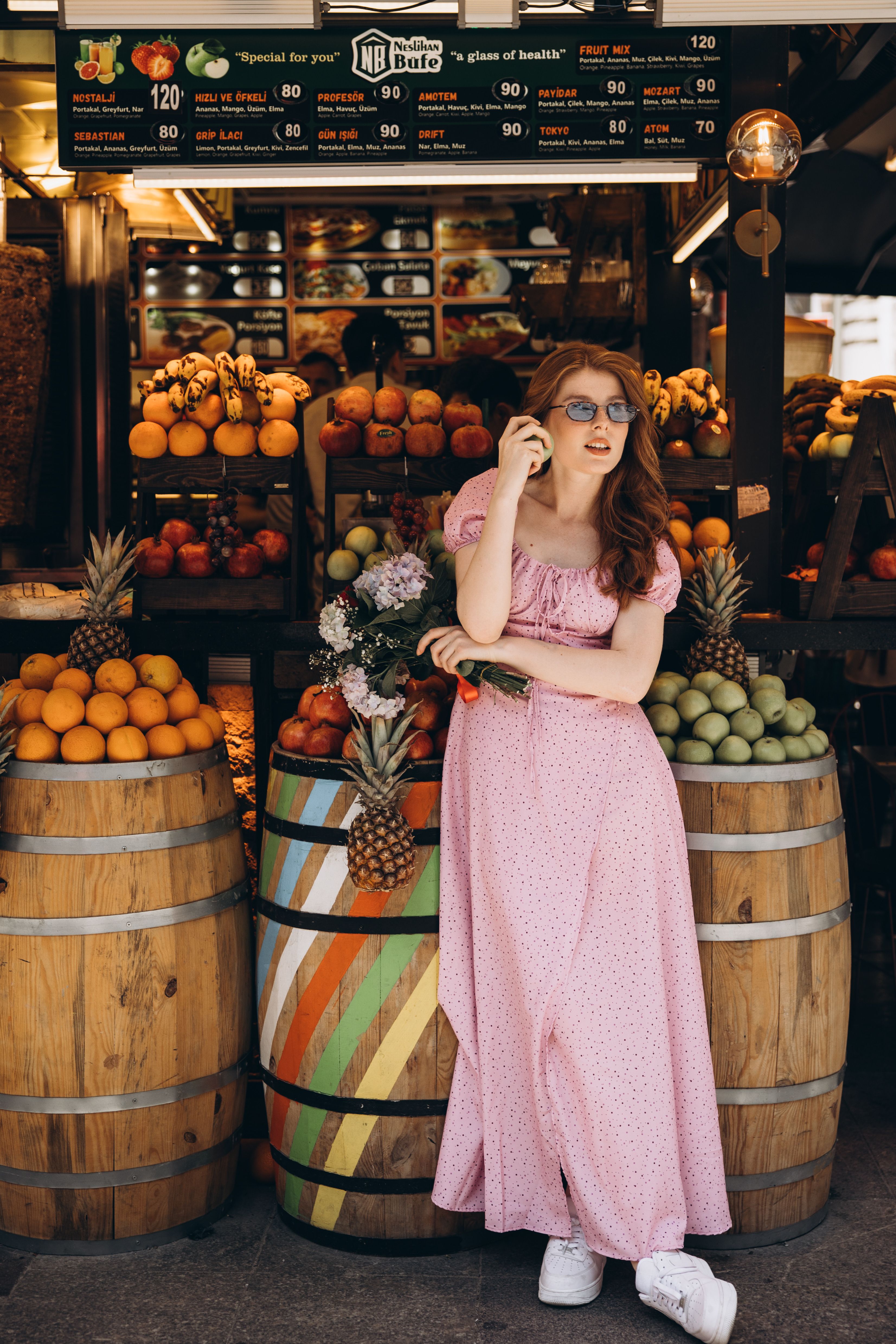 A woman in a pink dress stands in front of a fruit stand · Free Stock Photo