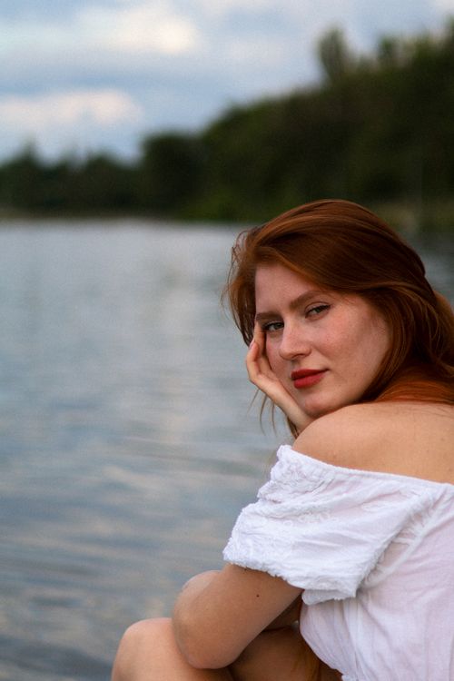 Free Close-up portrait of a redhead woman in a white blouse sitting by a lake. Stock Photo