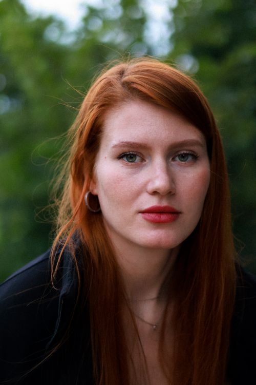 Free Portrait of a redhead woman with earrings against a natural outdoor background. Stock Photo