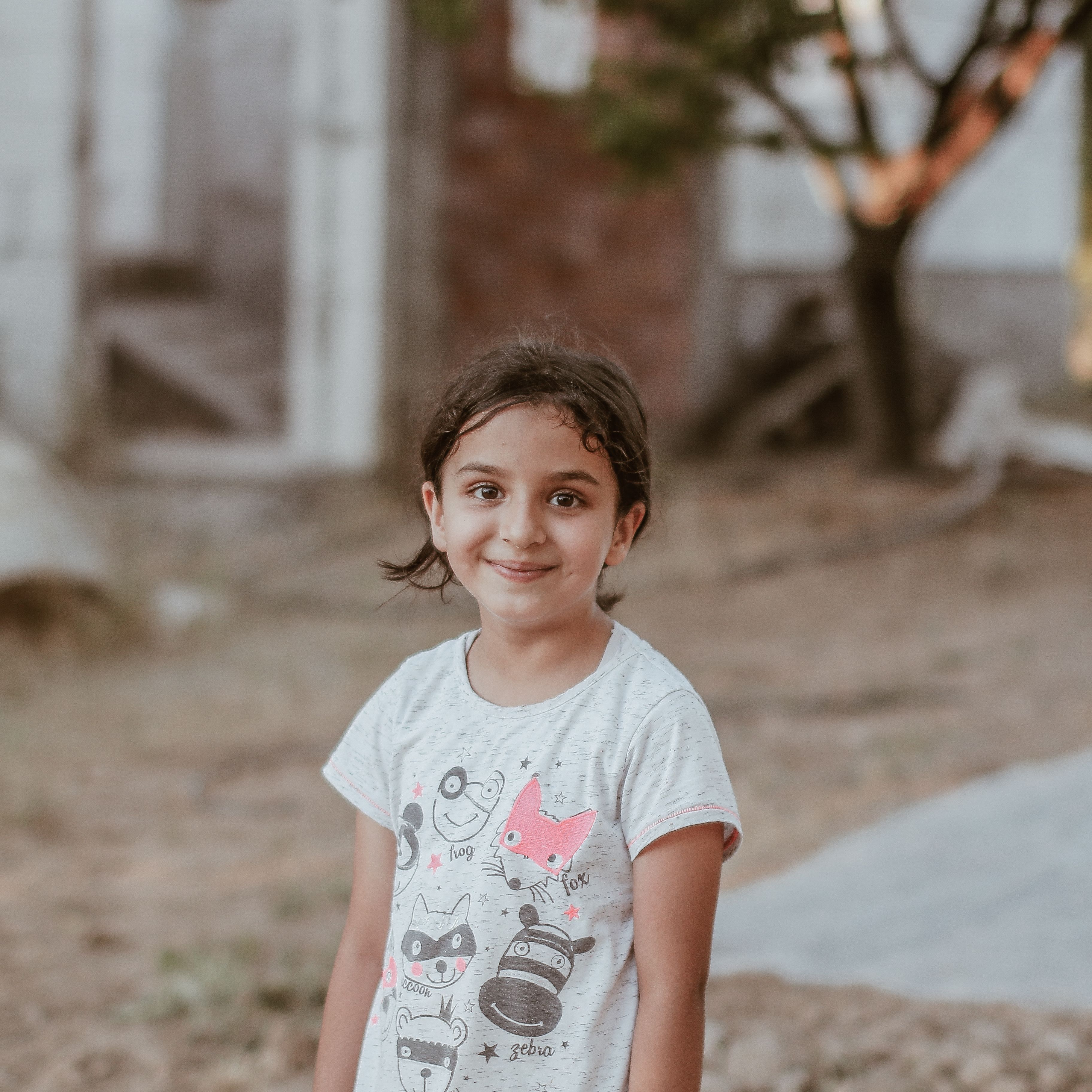 Cheerful young girl smiling in an outdoor setting, wearing a graphic t-shirt.