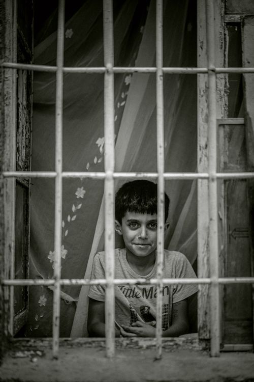 Free A black and white portrait of a boy smiling while peering through barred windows, creates a poignant moment. Stock Photo