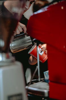 A barista skillfully pours coffee into a red cup at a cafe in Baku, creating a perfect coffee moment.