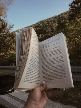 A person holds an open book against a scenic backdrop in Dubrovnik, Croatia, evoking a peaceful reading moment.