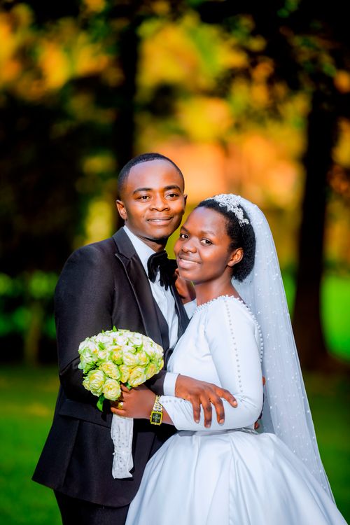 Free Joyful couple in wedding attire posing in a serene park setting. Stock Photo