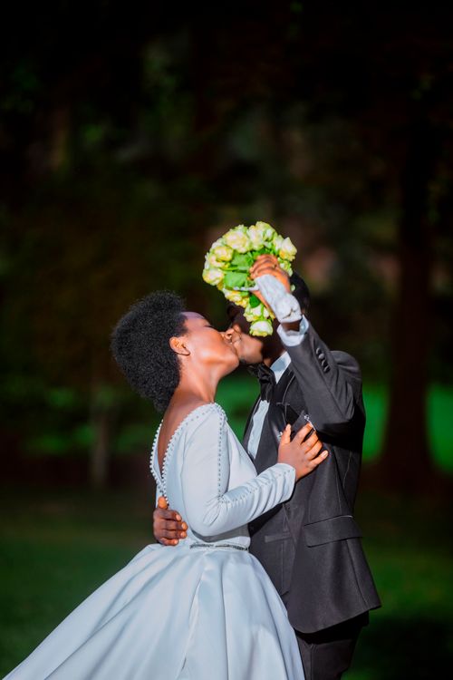 Free A newlywed couple shares a romantic kiss outdoors, capturing a tender wedding moment. Stock Photo
