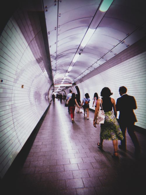 Free A group of people walking through a dimly lit subway tunnel with curved tiles. Stock Photo