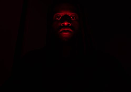 A dramatic portrait of a man illuminated by red light in complete darkness, creating a mysterious effect.