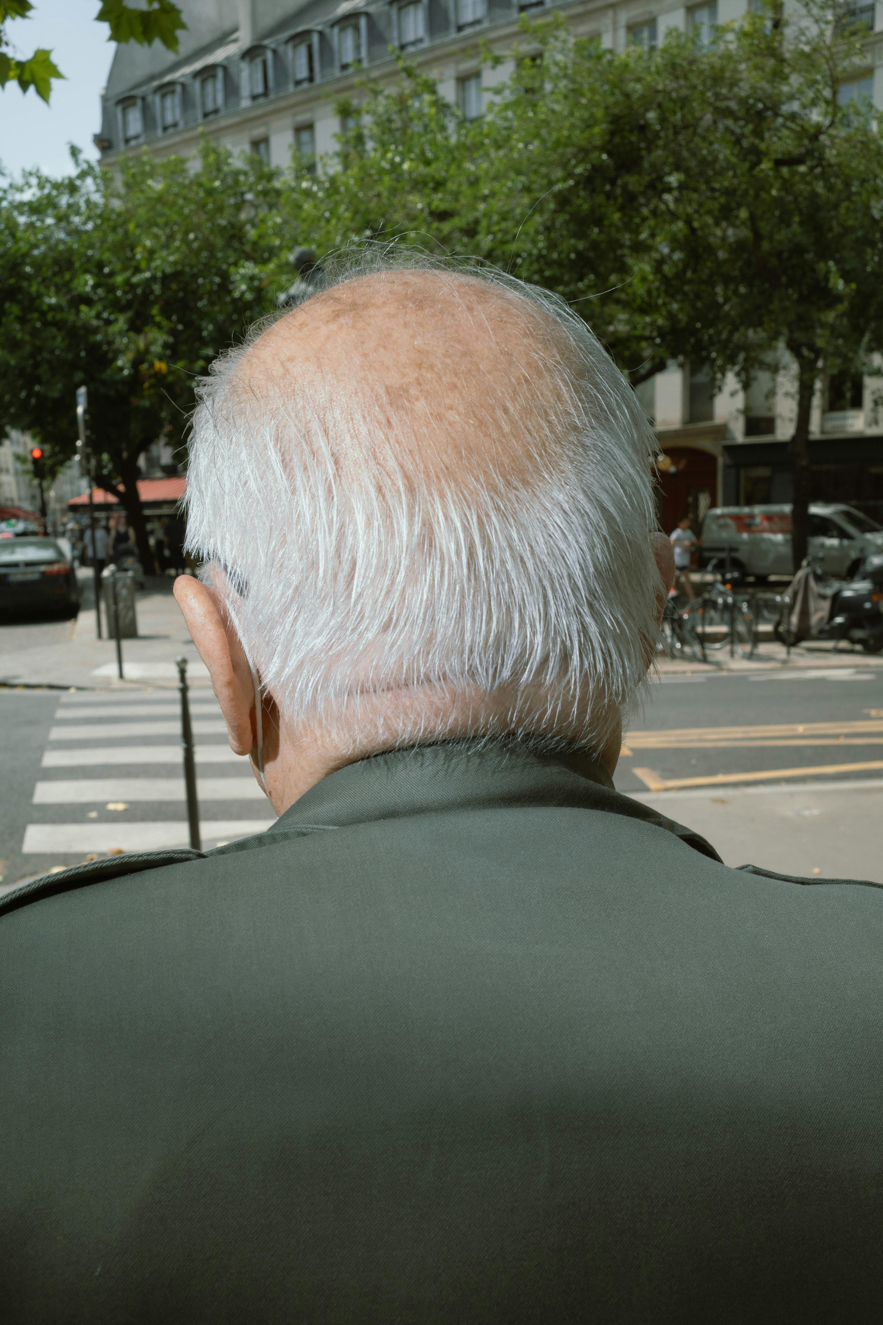 Rear view of an elderly man crossing a city intersection on a clear day.