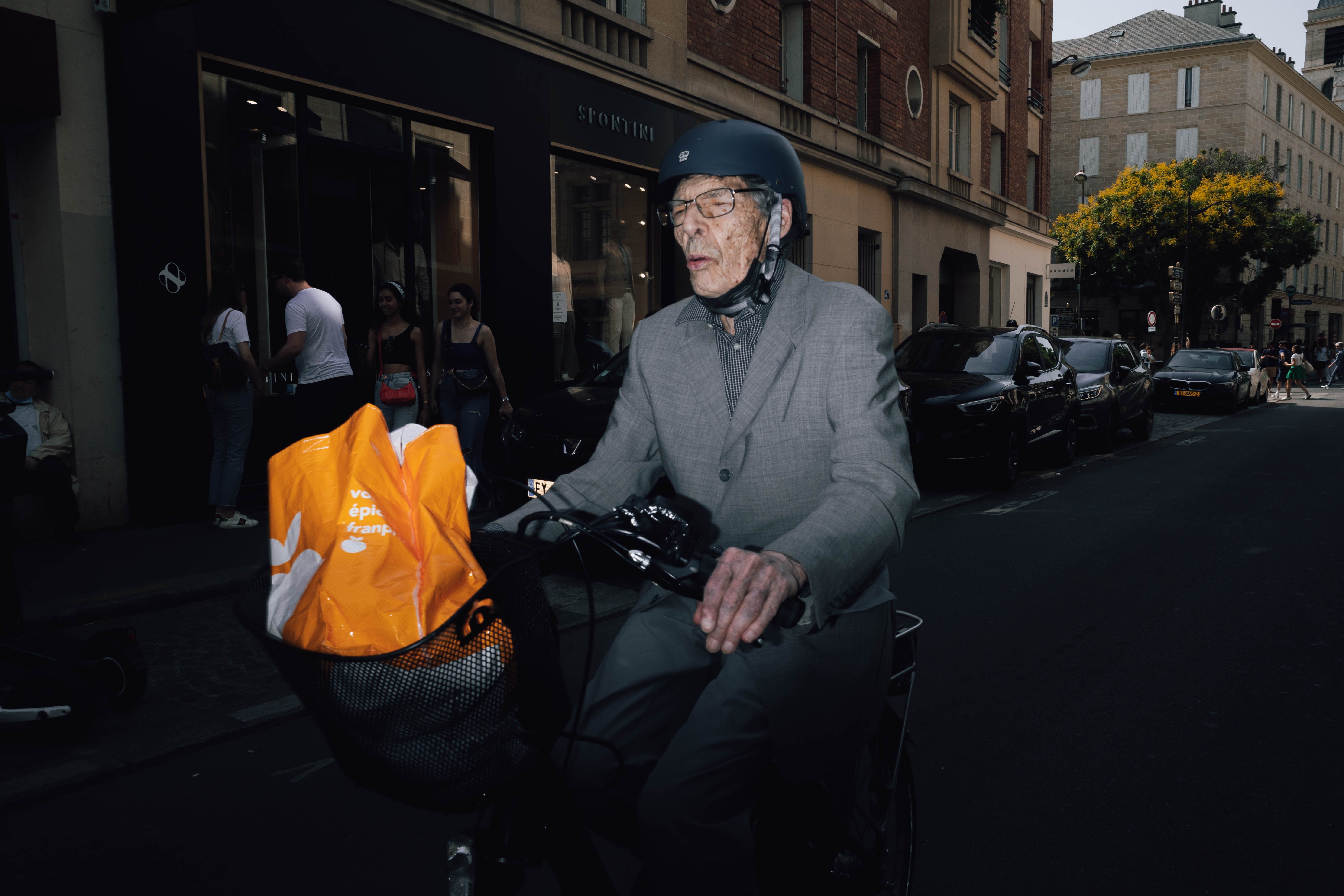 Senior man in a suit cycling on city streets with helmet, showcasing urban lifestyle.