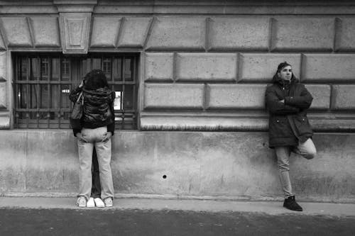A Couple and a Lonely Man Standing against the Wall on the Sidewalk 