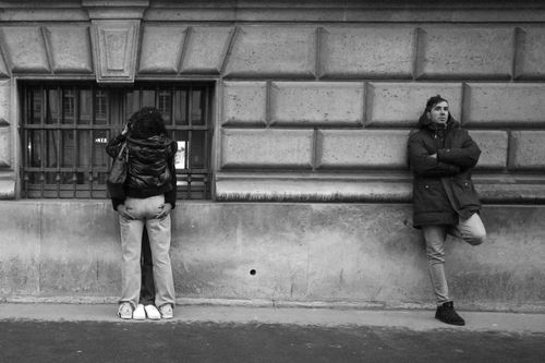 Free Black and white city scene depicting a couple hugging and a solitary man leaning against a wall. Stock Photo