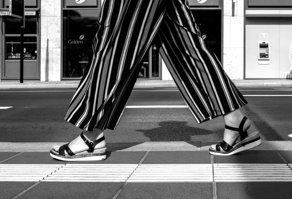Stylish woman in wide-leg trousers and structured blazer walking on a city sidewalk in summer