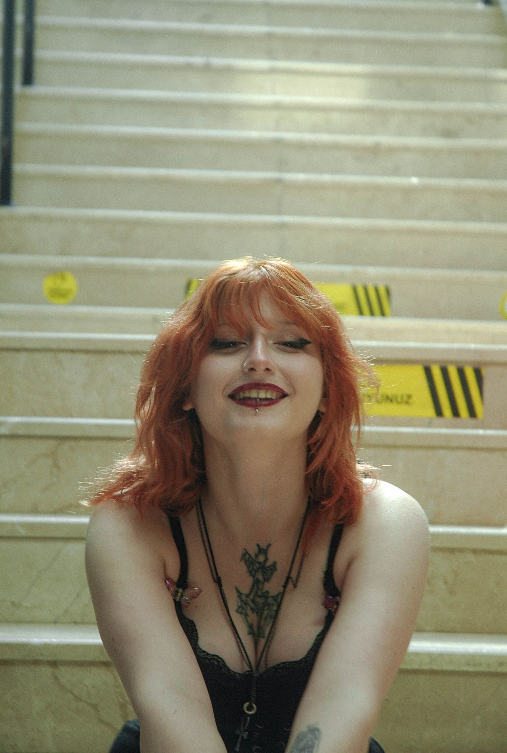 Redhead woman with tattoos smiling on stairs in İstanbul, Türkiye.
