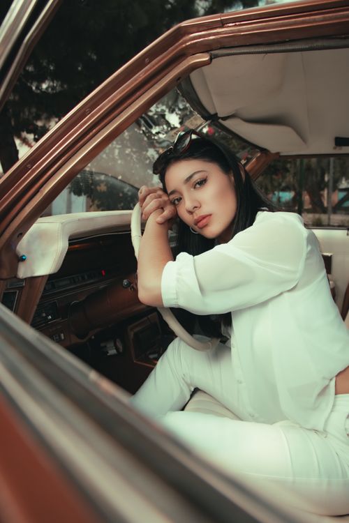 Free Young woman in white posing inside a car in Cochabamba, Bolivia, showcasing fashion and elegance. Stock Photo