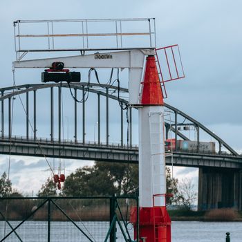 View of an industrial crane with a backdrop of a Lisbon bridge over the river.