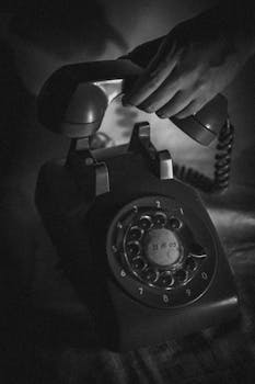 An artistic black and white photo of a hand lifting a vintage rotary phone, capturing nostalgia.