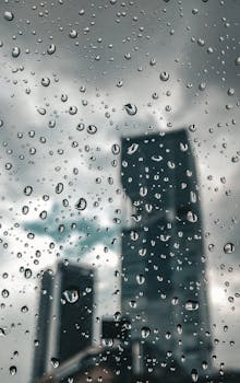 Raindrops on a window with an urban skyscraper in the background, creating a moody urban scene.